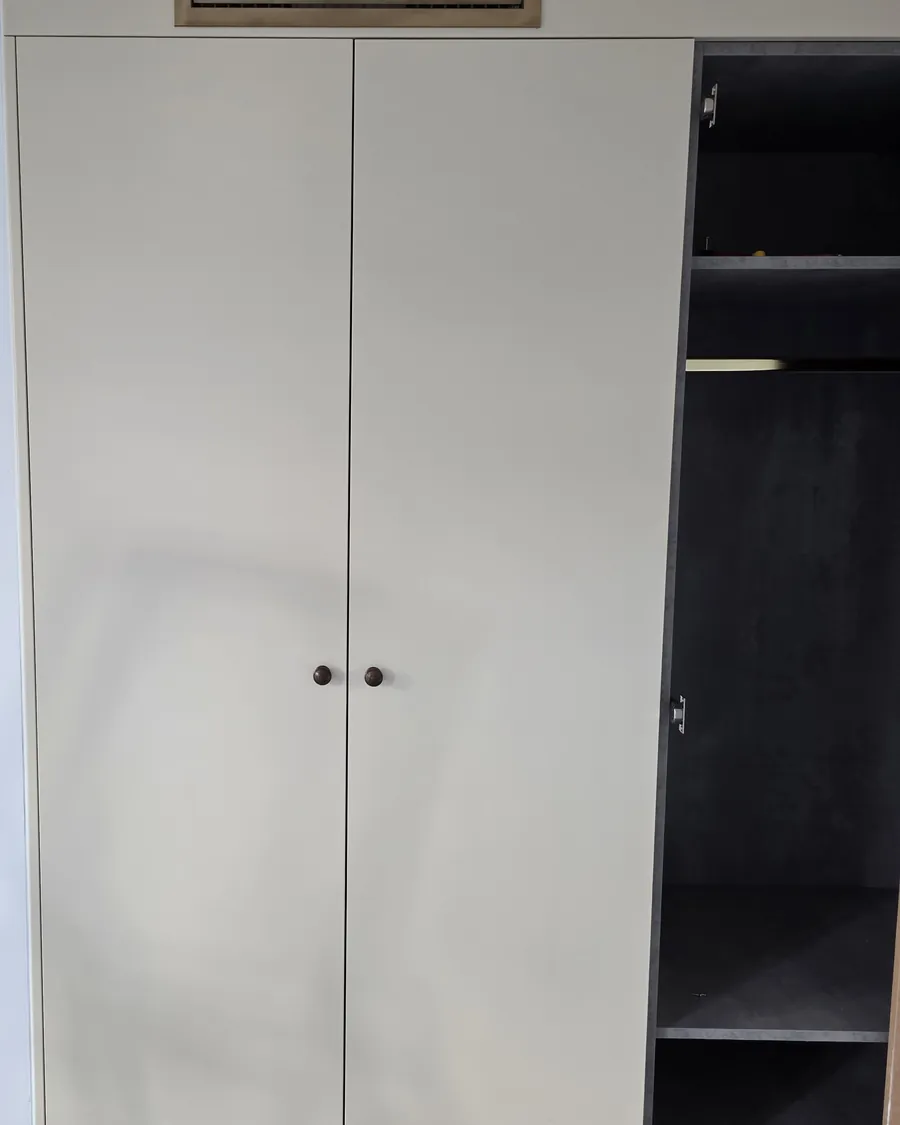 Finished built-in wardrobe with two painted doors and a brass air grille